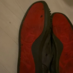 Gråa loubs med nitar och röd sula - Säljer ett par gråa Loubs med snörning och coola nitar över tån och runt hela skon. Skorna har en tydlig röd sula och är tillverkade i mocka. Perfekta för dig som vill sticka ut med din stil.