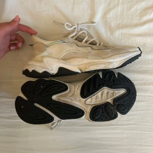 Vita Adidas Ozweego sneakers - Säljer ett par vita Adidas Ozweego sneakers med vit mesh och mockadetaljer. Skorna har chunky sula i svart och vitt samt snörning framtill. Perfekta för dig som gillar en sportig och trendig look.