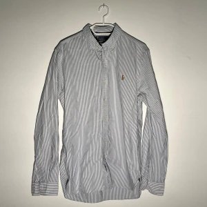 Randig skjorta från Polo Ralph Lauren - Klassisk blåvit randig skjorta från Polo Ralph Lauren i slim fit. Skjortan har långa ärmar, knappar framtill och broderad logga på bröstet. Perfekt för en stilren och tidlös look.