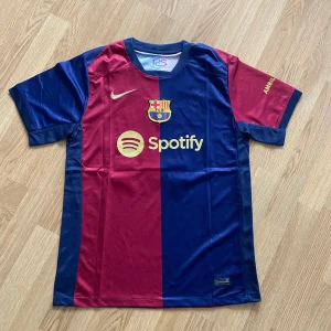 FC Barcelona matchtröja Lamine Yamal 19 - Säljer en officiell FC Barcelona fotbollströja med Lamine Yamal och nummer 19 på ryggen. Tröjan är kortärmad, har klassiska blå och röda vertikala fält, klubbmärke och Nike-logga framtill samt sponsortryck.