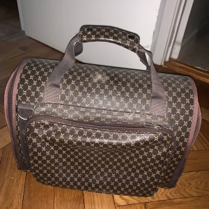 Transportväska för djur - Snygg och praktisk transportväska för katt eller liten hund  Säljer en stilren och bekväm transportväska som passar perfekt för katt eller liten hund (upp till ca 5-6 kg). Väskan är i fint skick och har ett lyxinspirerat mönster som påminner om designerväskor.  🟤 Stabil och lätt konstruktion 🟤 Två öppningar med nät för god ventilation 🟤 Mjuk insida för extra komfort 🟤 Bärhandtag + justerbar axelrem 🟤 Praktisk ytterficka för tillbehör  Perfekt för resor, veterinärbesök eller tåg/flyg. Väskan är a