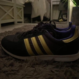 Svarta Adidas sneakers med gula ränder - Säljer ett par nya, svarta Adidas sneakers med klassiska gula ränder på sidorna och lila innerfoder. Perfekta för dig som gillar sportig stil och vill sticka ut lite extra. Storlek 38. Pris kan diskuteras❤️