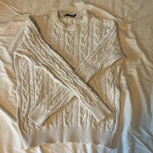 Vit kabelstickad tröja från 157 - Säljer en vit kabelstickad tröja från 157 i storlek M. Tröjan har rund halsringning och långa ärmar med ribbade muddar. Perfekt för lager-på-lager och ger en klassisk look med sitt stickade mönster.