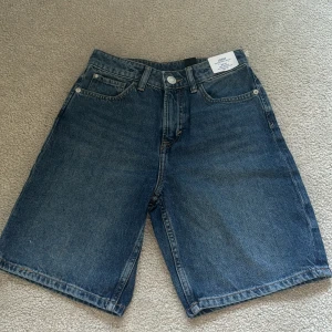 Blå jeansshorts med loose fit - Säljer ett par klassiska blå jeansshorts från Kappahl med loose fit och justerbar midja. Shortsen har fem fickor och normal längd, perfekta för en avslappnad stil.