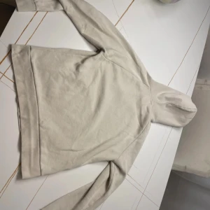 Beige hoodie med ficka - Säljer en stilren beige hoodie med huva och magficka. Tröjan har dragsko vid huvan och är tillverkad i mjukt material. Perfekt för en avslappnad look.