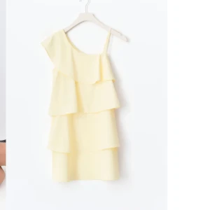 Ljusgul one shoulder klänning med volanger från Gina Tricot - Superfin slutsåld ljusgul klänning med one shoulder och flera lager volanger. Perfekt för sommarens alla tillfällen. Klänningen har en asymmetrisk axel och är tillverkad i ett lätt, syntetiskt material.
