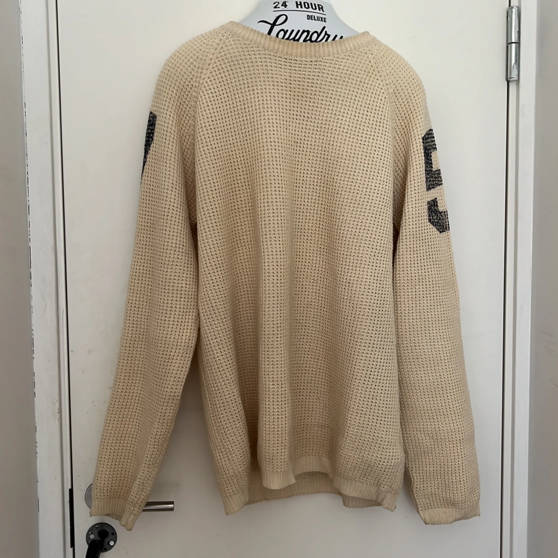 Beige stickad tröja med svarta siffror på ärmarna