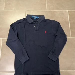 Mörkblå långärmad pikétröja från Ralph Lauren - Säljer en klassisk mörkblå långärmad pikétröja från Ralph Lauren med röd broderad logga på bröstet.