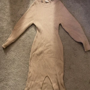 Beige ribbstickad långklänning från Stories - Säljer en beige ribbstickad långklänning från Stories i storlek S (36-38). Klänningen har lång ärm, rund halsringning och en snygg slits framtill. Perfekt för dig som gillar en enkel men stilren look. 