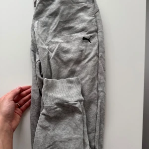 Grå hoodie från Puma set - Säljer en grå hoodie från Puma med dragkedja framtill och huva med snören. Tröjan har långa ärmar, två fickor fram och ribbade muddar vid ärmslut och nederkant. Perfekt för en avslappnad stil.