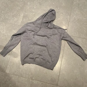 Grå merinoullhoodie med huva - Säljer en enkel och stilren grå hoodie med huva och dragsnören. Tröjan har långa ärmar och är tillverkad i mjukt material som passar perfekt för vardagsbruk eller när du vill vara extra bekväm.