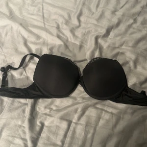 Svart bh med spetsdetaljer - Svart bh med vadderade kupor och fina spetsdetaljer upptill. Justerbara axelband och klassisk knäppning bak. Perfekt för dig som vill ha en enkel men ändå snygg bh.