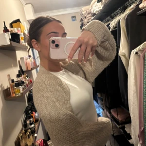 Beige stickad bolero från Gina Tricot - Säljer en beige stickad kofta från Gina Tricot. Koftan är croppad med lång ärm och har en mjuk, ribbad struktur. Perfekt att slänga över en topp för en avslappnad look.