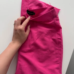 Chockrosa kostymbyxor från PrettyLittleThing - Säljer chockrosa kostymbyxor från PrettyLittleThing. Har en rak passform och är tillverkad i ett strukturerat syntetmaterial. Perfekt för dig som vill sticka ut med färg! 