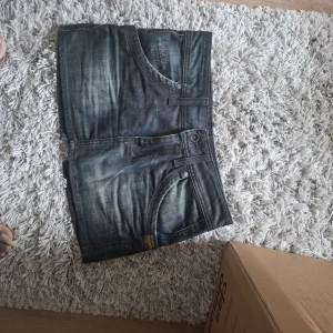 Mörkblå jeansskjolmed klassisk femficksdesign - Snygga mörkblå jeansshorts från G-Star RAW med klassisk femficksdesign och slitna detaljer. Shortsen har normal passform, knappgylf och tydliga sömmar. Perfekta för en avslappnad stil.
