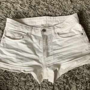 Vita jeansshorts från H&M - Säljer ett par vita jeansshorts från H&M med klassisk femficksdesign och knappgylf. Shortsen har låg midja och korta ben, perfekt för varma dagar. Snygg och enkel stil som passar till det mesta.