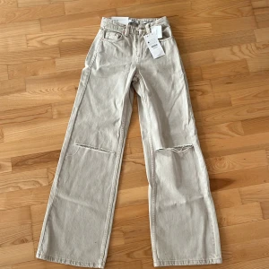 Beige wide leg jeans från Bershka - Säljer ett par beige wide leg jeans från Bershka med hög midja och raka, vida ben. Byxorna har klassisk femficksdesign och dragkedja med knapp. Perfekta för en avslappnad och trendig stil. Aldrig använda.