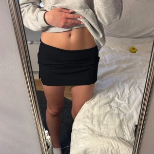 Svart ribbad minikjol - Säljer en svart ribbad minikjol med tight passform. Kjolen är kort och har en liten slits framtill. Perfekt för dig som gillar en enkel men stilren look.