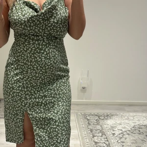 Grön blommig klänning med slits - Snygg grön klänning med små vita blommor och en draperad urringning. Klänningen är figurnära