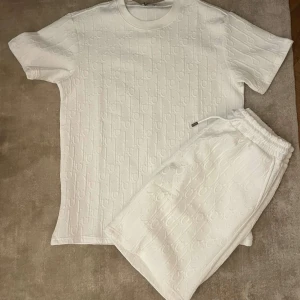  D short och t shirt  - Säljer ett par vita shorts från Dio med diskret mönster i tyget och snörning i midjan. Perfekta för sommaren och har en riktigt clean look med exklusiv känsla.