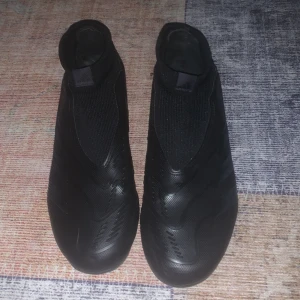 Svarta Adidas Predator fotbollsskor - Säljer ett par svarta Adidas Predator fotbollsskor med låg profil och strumpliknande skaft. Skorna har en slät ovandel utan snörning och är tillverkade i syntetmaterial. Perfekta för dig som vill ha bra grepp och kontroll på planen dem är också väldigt tajta dem är ganska nya knappt använda och dem är storlek 39 !OBS kan diskutera pris 