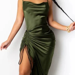 Olivgrön satinklänning med drapering - Snygg olivgrön satinklänning med smala axelband och draperad detalj på sidan som ger en cool slits. Klänningen har en cowlneck-ringning och är figurnära med en elegant glansig finish. Perfekt för dig som vill sticka ut!