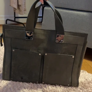 Grå handväska från Filippa K - Stilren grå handväska från Filippa K i mocka med två stora ytterfickor framtill och robusta handtag. Väskan har dragkedja upptill och detaljer i silverfärgad metall. Pris kan diskuteras vid snabb affär!