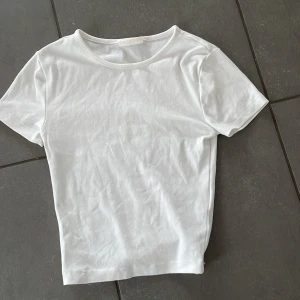 Vit basic t-shirt från Gina Tricot - En klassisk vit t-shirt från Gina Tricot, modell Basically Basics. T-shirten har rund halsringning och korta ärmar. Perfekt att matcha med jeans eller kjol för en enkel och stilren look.