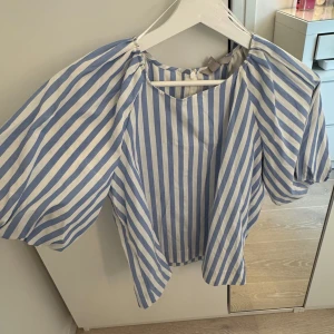 Blåvit randig blus från H&M - Säljer en blåvit randig blus från H&M med puffiga korta ärmar och rund halsringning. Blusen har ett luftigt och somrigt snitt, perfekt för varma dagar. Snygg att styla med jeans eller kjol!
