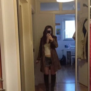 Brun fuskpälsjacka - Säljer en brun fuskpälsjacka som köptes i Spanien. Jackan har en mjuk och fluffig känsla, är lång och har en lös passform. Perfekt för att hålla sig varm och snygg under kallare dagar. Stängs framtill och har breda slag.