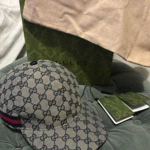 Gucci keps med monogram och röd-blå rand - Säljer en exklusiv keps från Gucci med klassiskt GG-monogram i navy blå. Kepsen har en röd och blå rand på sidan och justerbar rem baktill. Perfekt accessoar för att lyfta din stil.och så klart så kan priset diskuteras 