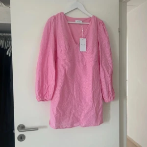 Rosa blommig kortklänning från Vila - Supersöt rosa klänning från Vila med v-ringning och långa puffärmar. Klänningen har broderade blommor i tyget och är i kort modell. Perfekt för vår och sommar!