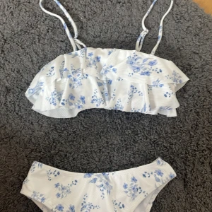 Vit blommig bikini med volang - Jättefin oanvänd ny bikini med volangdetaljer och smala axelband💕 Vit botten med ljusblå blommigt mönster. Fin underdel (inte string)!💗 Från SHEIN men bra skick!❤️