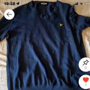 Mörkblå tröja från Lyle & Scott - Snygg mörkblå tröja från Lyle & Scott med klassisk gul logga på bröstet. Tröjan har rund halsringning och långa ärmar, samt ribbade muddar vid ärmslut och nederkant. Perfekt för en stilren och enkel look.