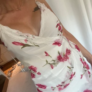 blommig omlottklänning från Zara storlek S - Söt vit kortklänning med rosa blommigt mönster och spets längs v-ringningen. Omlottmodell med knyt i midjan och tunna axelband. Från Zara, storlek S. Använd en gång! 