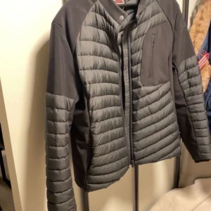 Svart quiltad jacka från Colmar - Snygg svart quiltad jacka från Colmar med dragkedja och hög krage. Jackan har en bröstficka med dragkedja och diskret logga på ärmen. Perfekt för kyliga dagar och stilren look.