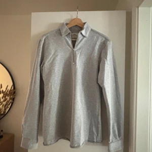 Grå långärmad pikétröja med dragkedja - Säljer en stilren grå långärmad pikétröja med krage och dragkedja framtill. Storlek S, märke Ciszere