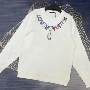 Vit sweatshirt från Louis Vuitton - Vit sweatshirt med färgglad Louis Vuitton-logga tryckt runt halsen och ett litet tryck av en väska framtill. Tröjan har rund halsringning och långa ärmar. Perfekt för en trendig och avslappnad stil.
