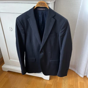 Oscar Jacobsson kavaj  - Säljer en riktigt stilig kavaj ifrån Oscar Jacobsson. Den är i storlek S och är normal i storlek. Nypris i butik 4000kr✅pruta vid snabb affär. Någon blandning av svart och mörkblå 