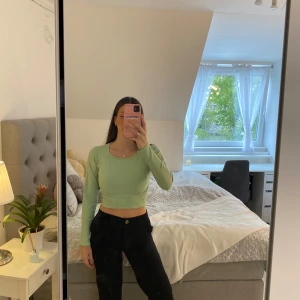 Ljusgrön croppad långärmad topp - Säljer en ljusgrön croppad topp med långa ärmar. Toppen har ribbade detaljer vid midjan och ärmarna, och en rund halsringning. Perfekt för dig som gillar en tight passform och stilren look.