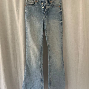 Ljusblå bootcut jeans med knappar - Säljer ett par ljusblå jeans med bootcut-modell och hög midja. Jeansen har flera knappar framtill och klassiska fickor både fram och bak. Perfekta för dig som gillar en retroinspirerad stil.
