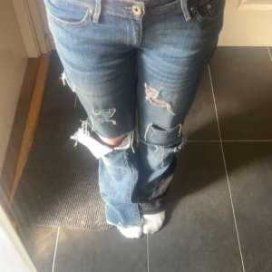 Lågmidjade jeans  - Säljer ett par blå jeans med flera slitningar och hål på benen. Dem är sydda lågmidjade och utsvängda❤️