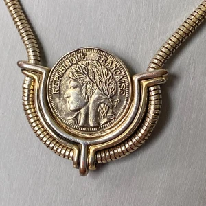 Vintage halsband med fransk myntberlock - Unikt vintage halsband i guldtonad metall med en stor fransk myntberlock. Halsbandet har en ormlänk och myntet visar en klassisk profil med lagerkrans och texten 'République Française'. Baksidan har ett vackert vapensköldmotiv. Statement piece med cool retrovibe.