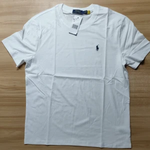 Vit t-shirt från Polo Ralph Lauren - Klassisk vit t-shirt från Polo Ralph Lauren med broderad marinblå logga på bröstet. T-shirten har rund halsringning och korta ärmar. Tillverkad i mjuk bomull för en skön och stilren look. Perfekt till jeans eller shorts för en clean vibe. Storlek är L men passar som M. Vid minsta fundering är det bara att skicka ett dm:)