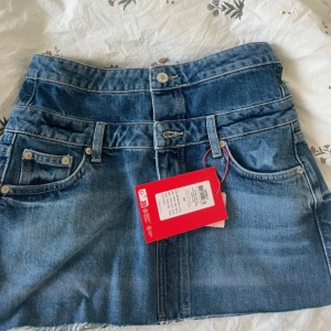 Blå jeanskjol från Only - Snygg blå jeanskjol från Only med klassisk femficksdesign, rå kant nertill och bälteshällor. Kjolen har en normal passform och stängs med knapp och dragkedja framtill. Perfekt till sneakers eller boots.
