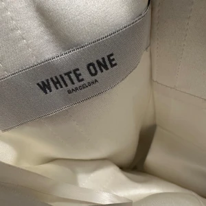 Vit brudklänning White One Barcelona storlek 38 - Drömmig lång brudklänning från White One Barcelona i vit satin och tyll. Klänningen har axelbandslös överdel, vackra spetsdetaljer med pärlor och en vid kjol som ger en riktigt prinsesskänsla. Knappar längs ryggen och romantiska broderier gör den extra speciell. Brudslöja medföljer.  Klänningen behöver kemtvätts. Vid snabb affär kan priset diskuteras. 