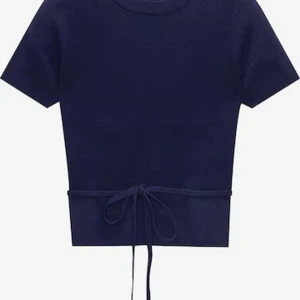 Mörkblå stickad topp från Pull&Bear - Mörkblå stickad topp från Pull&Bear med korta ärmar och rund hals. Snygg detalj med knytband i midjan som ger en cool och modern look. Perfekt till jeans eller kjol för en avslappnad stil.