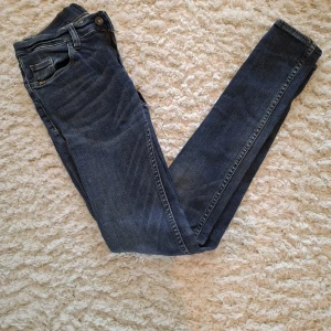 Blå jeans från Tiger of Sweden - Snygga blå jeans från Tiger of Sweden med klassisk femficksdesign och ljusa slitningar. Modellen har smal passform och raka ben, med normal midja och dragkedja. Perfekta till sneakers eller boots för en clean look.