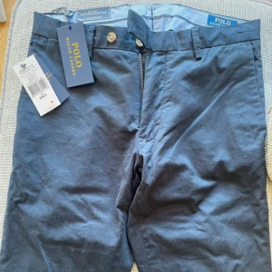 Mörkblå chinos från Polo Ralph Lauren - Säljer mina snygga mörkblå chinos från Polo Ralph Lauren i stretchigt bomullsmaterial då de tyvärr är försmå för mig. Nypris är ca 2000 kr. Endast provtestade, helt i nyskick prislapp finns med.  Slim fit-modell med klassisk design, bälteshällor och dragkedja. Perfekta för en clean och stilren look. Storlek 29/32. Vi fler frågor eller funderingar hör gärna av er! 