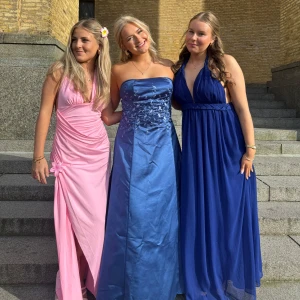 Marinblå långklänning med flätade band - Säljer en marinblå långklänning med djup v-ringning och flätade axelband som knyts i nacken. Klänningen har ett markerat midjeband med flätad detalj och ett luftigt, svepande tyg. Perfekt för bal eller student! Snygg och elegant look.